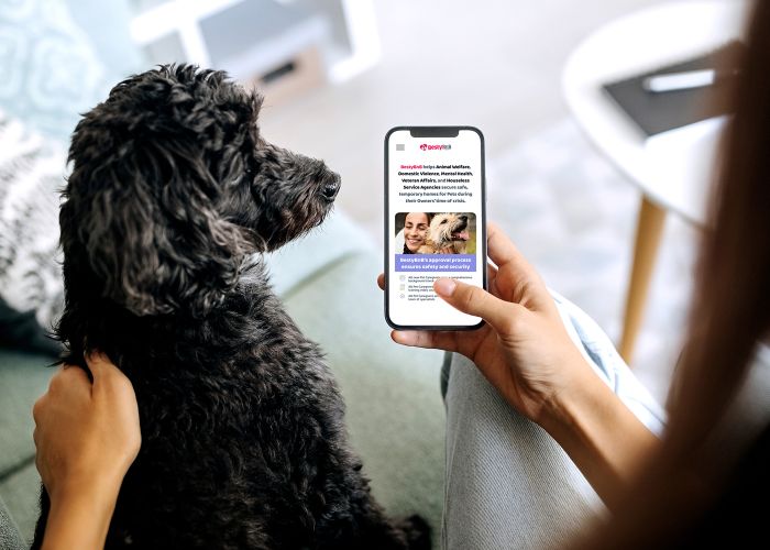 Woman holding a smartphone next to a black dog.