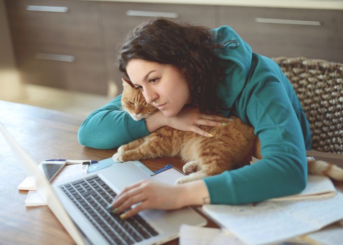 Sad woman hugging a cat while on her laptop computer.