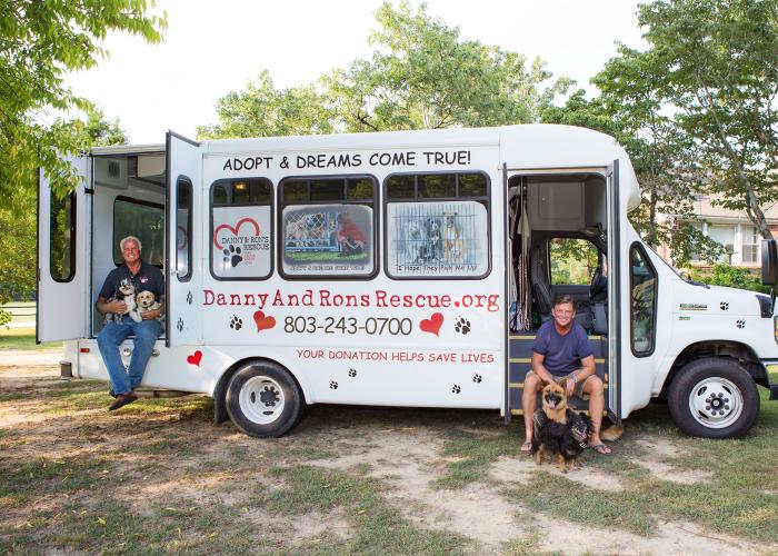 two men and their dogs sit alongside their rescue bus