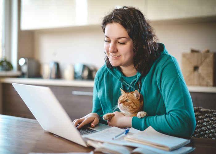 a woman holding a cat on her lap while looking at her laptop