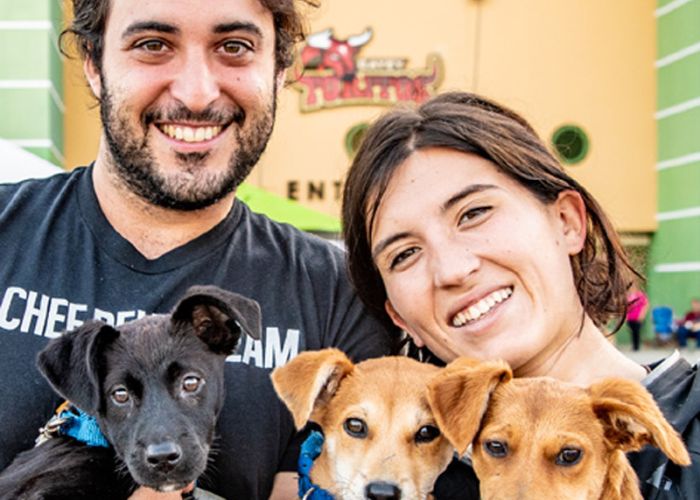 a man and a woman smile as they hold up three puppies