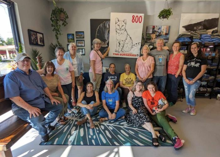 a group of smiling people gathered around a sign that says 800 TNR surgeries