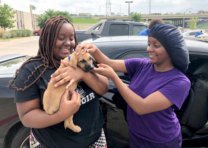 one woman holds a puppy while another examines its head