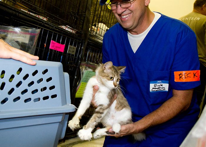 A man smiles as he transfers a small cat into a carrier